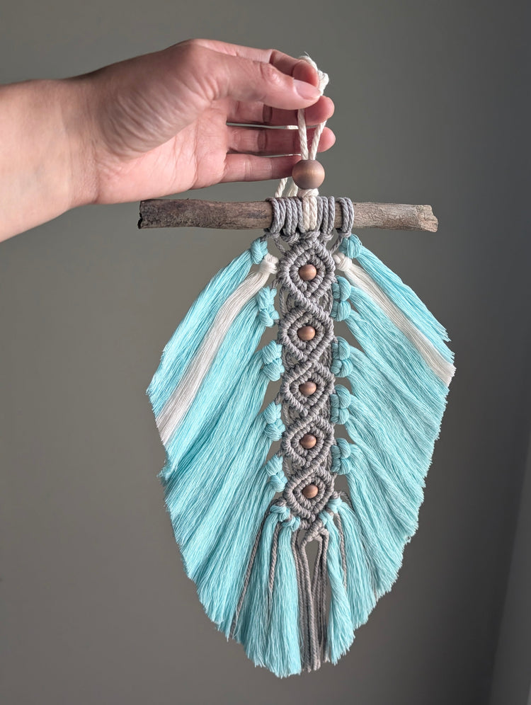 Decorative feather with braided top held by a hand against a plain background