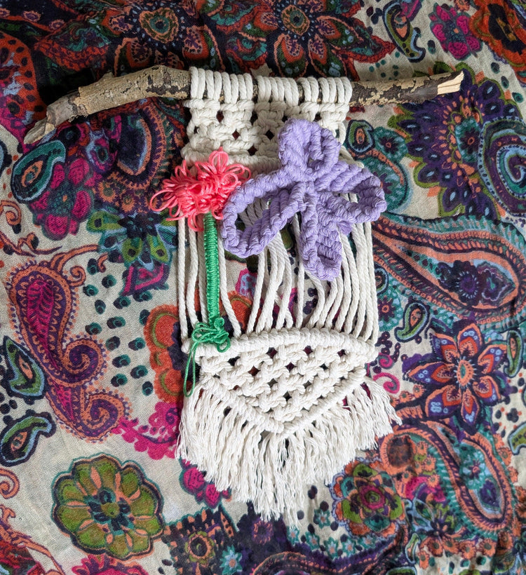 Macrame wall hanging with colorful flowers on a patterned fabric background