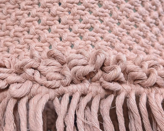 Brown knitted lampshade with fringe on a chair against a neutral background