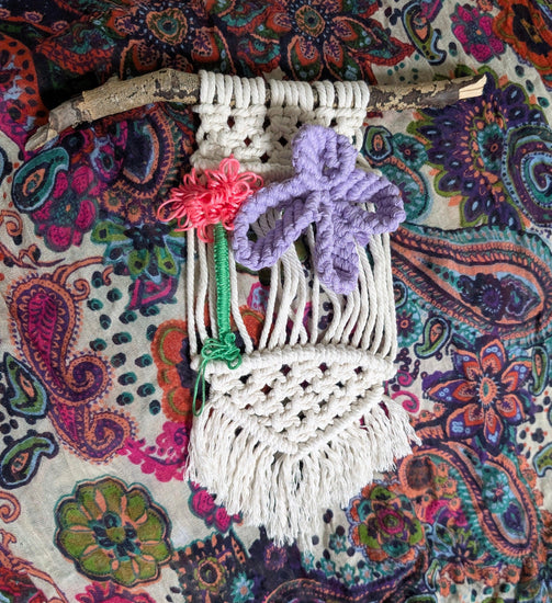 Macrame wall hanging with colorful flowers on a patterned fabric background