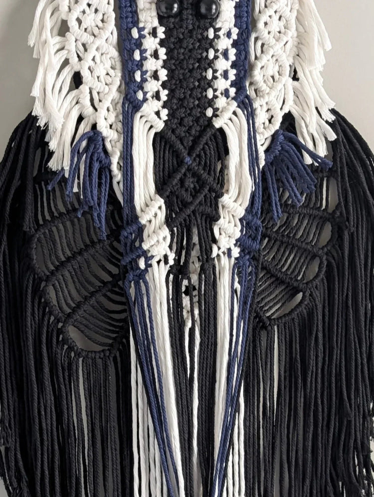 Decorative wall hanging with black and white fringes on a gray wall.