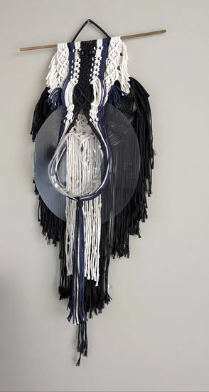 Decorative wall hanging with black and white fringes on a plain wall.