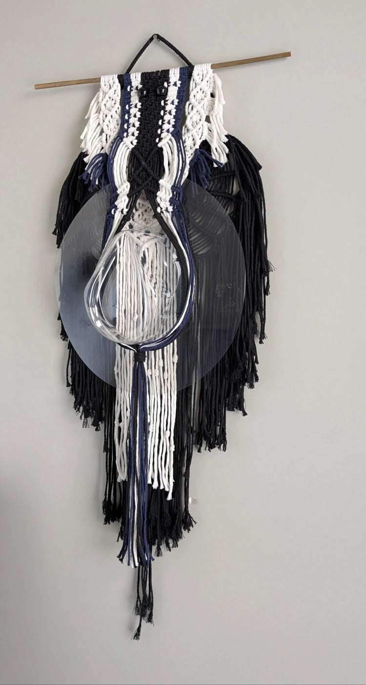 Decorative wall hanging with black and white fringes on a plain wall.